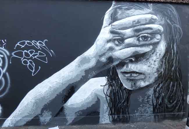 Street art shows girl looking through fingers.