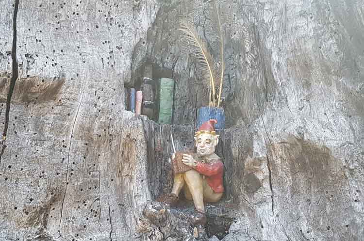 An elf sitting beneath a bookcase reading a book.