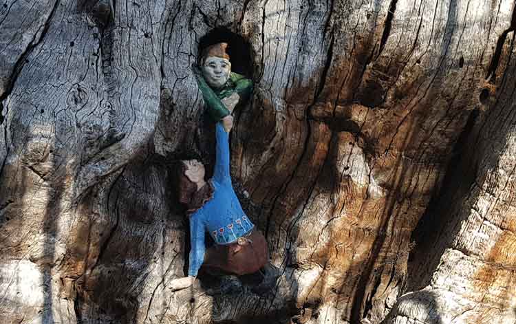An elfin figure helps another climb up the tree
