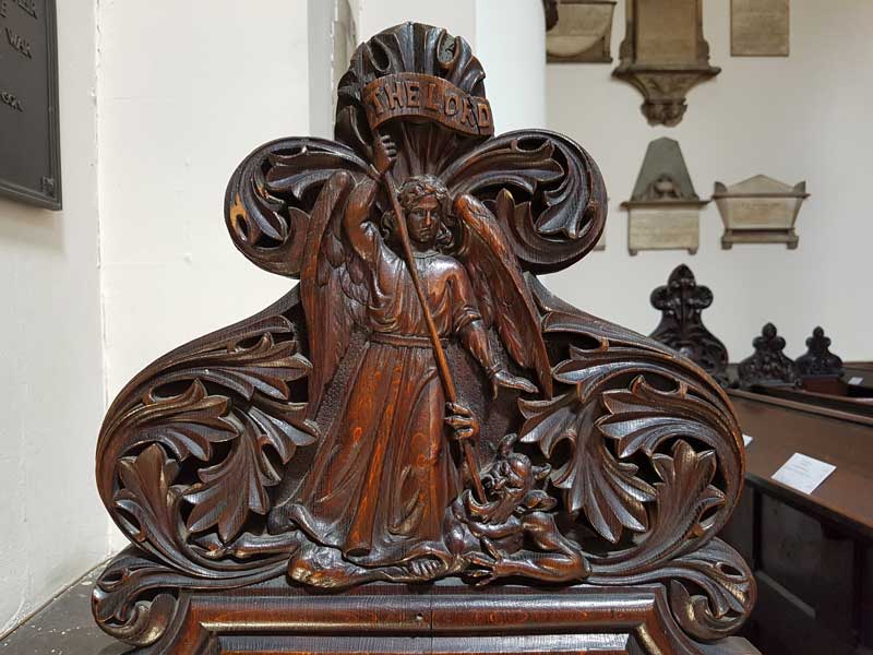 The carving on the church wardens pew showing St Michael driving a spear into the devil's mouth.