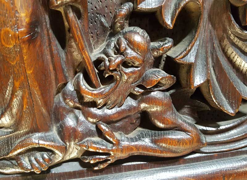 A close-up of the devil's face on the churchwarden's pew.